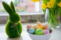 White bowl with colored easter eggs, bouquet of yellow tulips and daffodils flowers and green bunny rabbit on white kitchen table