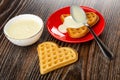 Bowl with condensed milk, spoon in red saucer with heart shaped cookies poured condensed milk on table Royalty Free Stock Photo