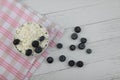 White bowl of farmer cheese on red and white napkin and a pile of blueberry on white wooden background flat lay. Healthy