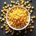White bowl filled with yellow corn kernels rests on dark surface. Scattered corn kernels surround bowl, creating visually Royalty Free Stock Photo