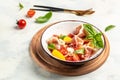 White bowl of fresh and healthy Mediterranean salad with tomatoes, cream cheese balls, prosciutto jamon and basil leaves. Royalty Free Stock Photo