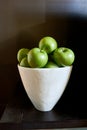 A white bowl full of green Granny Smith apples against a brown wall and table.