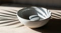 White bowl with a gray stone inside sits in sunlight with leaf shadows. Royalty Free Stock Photo