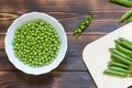 White bowl with green peeled peas inside on dark wooden table