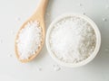 White bowl with large sea salt, wooden spoon, scattered salt cry