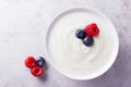 A white bowl with plain yogurt and some ripe blueberries and raspberries on grey countertop