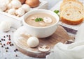 White bowl plate of creamy chestnut champignon mushroom soup on white kitchen background and box of raw mushrooms and fresh bread Royalty Free Stock Photo