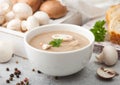 White bowl plate of creamy chestnut champignon mushroom soup on white kitchen background and box of raw mushrooms and fresh bread Royalty Free Stock Photo