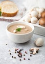 White bowl plate of creamy chestnut champignon mushroom soup on white kitchen background and box of raw mushrooms and fresh bread Royalty Free Stock Photo