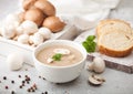 White bowl plate of creamy chestnut champignon mushroom soup on white kitchen background and box of raw mushrooms and fresh bread Royalty Free Stock Photo