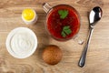 Bowl with sour cream, salt, transparent bowl with borsch, bun, spoon on wooden table. Top view