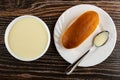 Bowl with sweet condensed milk, bun and spoon with condensed milk in plate on wooden table. Top view Royalty Free Stock Photo