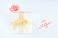 White box with gift inside wrapped in gold ribbon with abow, on the box lies pink rose in front of white background. Holiday gift