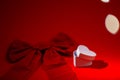 A white box in the shape of a heart stands on a bright red background near a huge red bow for Valentine's Day on Royalty Free Stock Photo