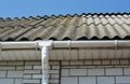 White brick house with repaired old and new asbestos roof sheets and plastic rain gutter pipeline