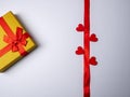 On a white bright background lies a long red ribbon surrounded by four hearts and next to a yellow gift Royalty Free Stock Photo