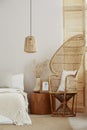 White and bright interior with wicker peacock chair with white pillow, rattan lamp and wooden nightstand with frame with