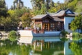 A white and brown Chinese pavilion in the garden with people walking through the pavilion near a deep green lake with lush green t Royalty Free Stock Photo