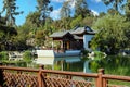 A white and brown Chinese pavilion in the garden with people walking through the pavilion near a deep green lake with lush green t Royalty Free Stock Photo