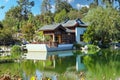 A white and brown Chinese pavilion in the garden with people walking through the pavilion near a deep green lake with lush green t Royalty Free Stock Photo