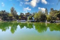 A white and brown Chinese pavilion in the garden with people walking through the pavilion near a deep green lake Royalty Free Stock Photo