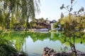 A white and brown Chinese pavilion in the garden with people walking through the pavilion near a deep green lake Royalty Free Stock Photo