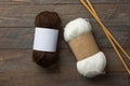 White and brown skeins of hand spun yarn with blank Kraft paper wrap labels for mockup on rustic wooden table with needles.