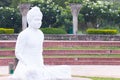 A white Buddha statue defocused in the foreground with green plants and concrete structures behind Royalty Free Stock Photo