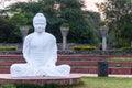 A white Buddha statue in meditation and defocused against  green trees of the park Royalty Free Stock Photo