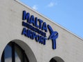 The white building of the Malta International Airport with arch windows and a big blue banner sign on the wall. Airport is close