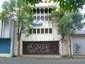 a white building with vandalized brown folding doors, windows and trees in front in the daytime