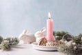 White bunnies, burning pink  candle , fir tree branches, decorative golden cones on white marble background Royalty Free Stock Photo