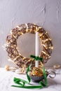 White burning candle, shiny glass cones, rustic wreath with bright fairy ligts
