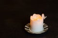 White burning pillar candle standing on gold decorated saucer on dark dining table