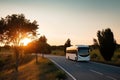 A white bus drives along a suburban road against the backdrop of a summer sunset. Generative ai Royalty Free Stock Photo