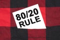 White business card with text 80 on 20 rule lies in the sleeve of a checkered shirt