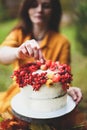 White cake with berries, maple leaves, apples, rowan. Woman in yellow dress on wooden chair by round table with blue tablecloth, Royalty Free Stock Photo