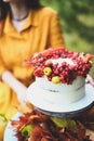 White cake with berries, maple leaves, apples, rowan. Woman in yellow dress on wooden chair by round table with blue tablecloth, Royalty Free Stock Photo