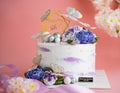 White cake with butterfly and flower decorations on a pink background