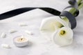 White calla flowers tied with a black mourning ribbon next to a burning candle with capsules and tablets on a white background. Royalty Free Stock Photo