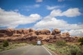 White Camper Van Drives Toward Red Rock Formation At Arches National Park In Utah USA