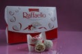 white candies round and halves in the background is a square rectangular gift box Raffaello stands on a pink fuchsia background si