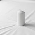 White candle with a black wick is placed on a smooth white fabric Royalty Free Stock Photo