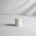 White candle is centered on a smooth, white fabric surface. The Royalty Free Stock Photo