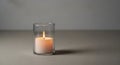 A white candle is lit and placed in a clear glass holder on a smooth gray surface. The flame is Royalty Free Stock Photo
