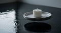 A white candle placed on a round, gray dish floats on a calm water surface. Ripples emanate gently Royalty Free Stock Photo