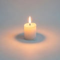 White candle sits on a plain surface, casting a warm glow and soft Royalty Free Stock Photo