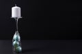 White candle on the stem of a champagne glass with blue Christmas balls on a black background Royalty Free Stock Photo