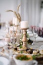 White candle on wooden candlestick , table is full of food and dishes , selective focus