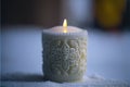 a white candle with a yellow candle light in it\'s center on a white surface with snow around it